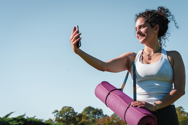 junge frau, die ein selfie mit einer rosa yogamatte macht, die über ihr schulterlebensstilkonzept drapiert ist