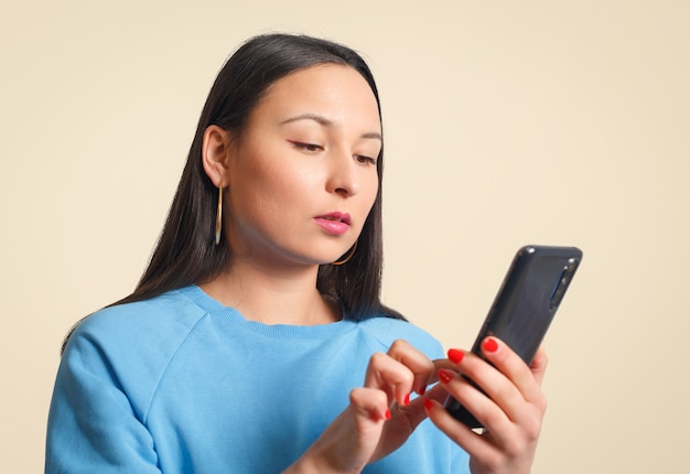 Junge Frau, die ein Smartphone benutzt. Auf einem cremefarbenen Hintergrund.