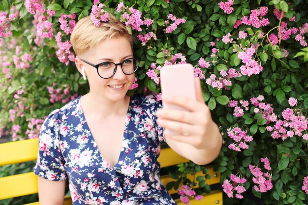 Junge Frau, die ein Smartphone nahe einem Blumenbusch benutzt