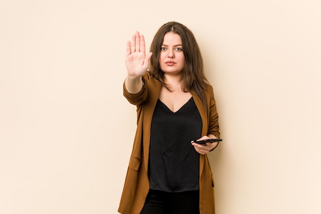 Junge Frau, die ein Telefon steht mit der ausgestreckten Hand zeigt das Stoppschild und verhindert Sie hält.