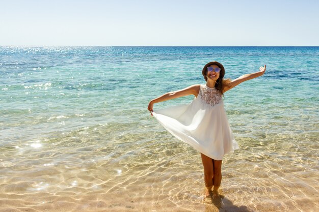 Junge Frau, die ein weißes Kleid und einen Hut stehen auf einem Strand und genießen die Sonne trägt