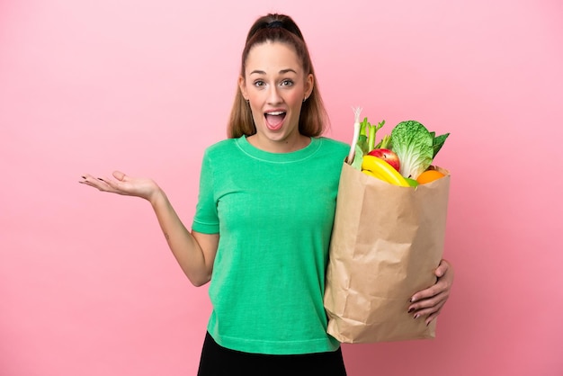 Junge Frau, die eine Einkaufstasche des Lebensmittels mit schockiertem Gesichtsausdruck hält