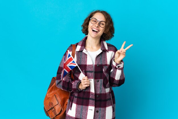 Junge Frau, die eine Flagge des Vereinigten Königreichs hält, die lokal gegen die leere Wand aufwirft