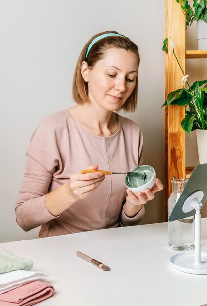 Junge Frau, die eine Gesichtsmaske aus blauem Ton anwendet, die Spa-Verfahren durchführt Gesichtspflegekonzept