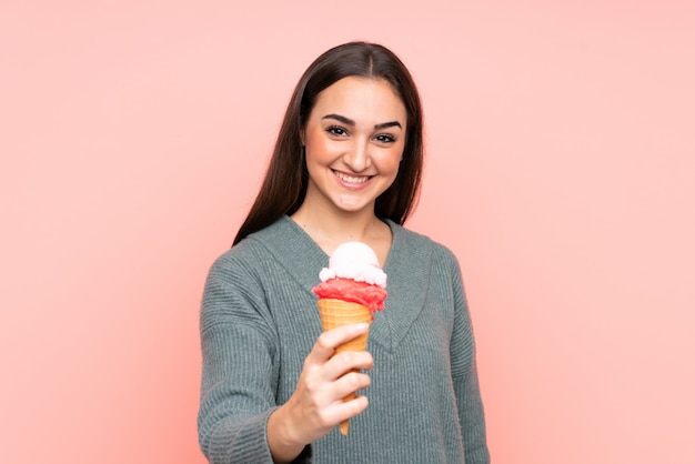 Junge Frau, die eine Kornett-Eiscreme lokalisiert auf rosa Wand mit glücklichem Ausdruck hält