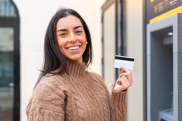 Junge Frau, die eine Kreditkarte im Freien hält und viel lächelt