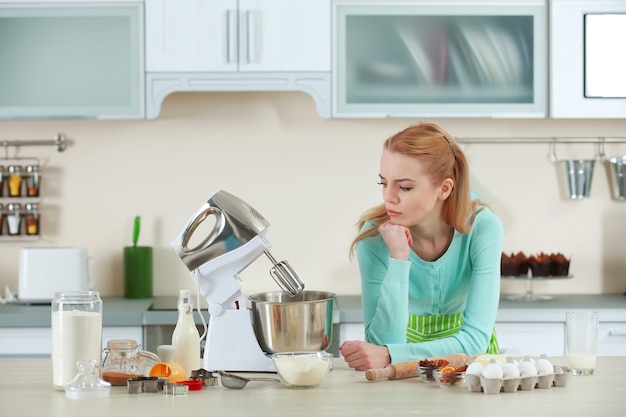 Junge Frau, die eine Küchenmaschine verwendet, um einen Teig zu machen