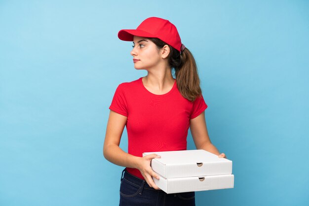 Junge Frau, die eine Pizza über der lokalisierten rosa Wand schaut Seite hält