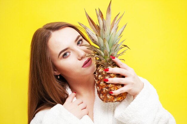 Junge Frau, die eine reife Ananas nahe ihrem Gesicht hält.