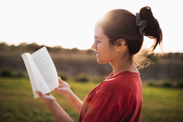 Junge Frau, die eine schöne Lesung hat, während sie lächelt und das Licht eines Sonnenuntergangs in einem Park genießt?