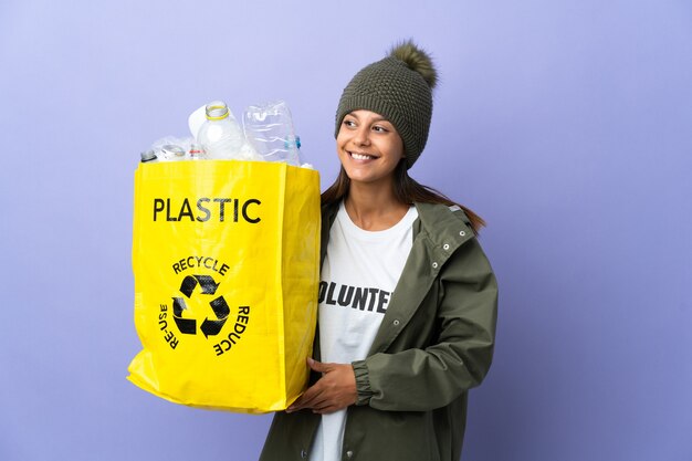 Junge Frau, die eine Tasche voll Plastik hält, die zur Seite schaut und lächelt