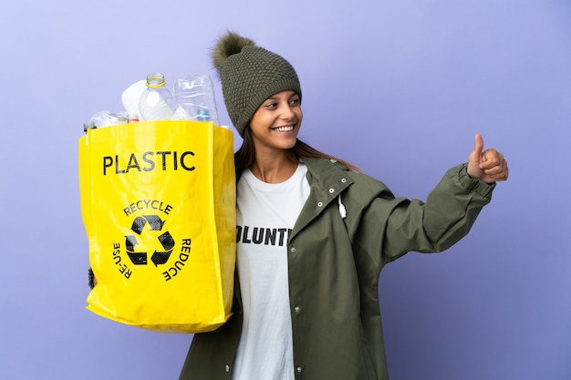 Junge Frau, die eine Tasche voll Plastik hält und eine Daumen hoch Geste gibt