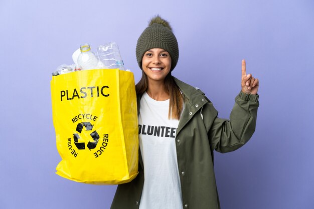 Junge Frau, die eine Tasche voll Plastik hält und einen Finger im Zeichen des Besten hebend zeigt