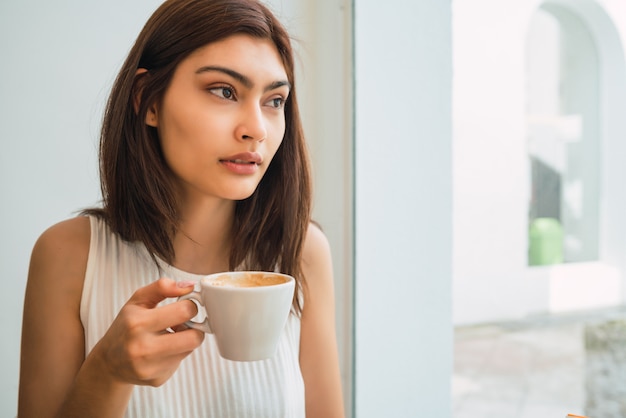 Junge Frau, die eine Tasse Kaffee am Kaffeehaus trinkt.