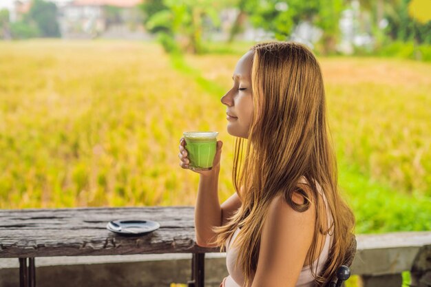 Junge Frau, die eine Tasse Matcha Latte, grüner Tee, auf einem alten hölzernen Hintergrundtisch hält.
