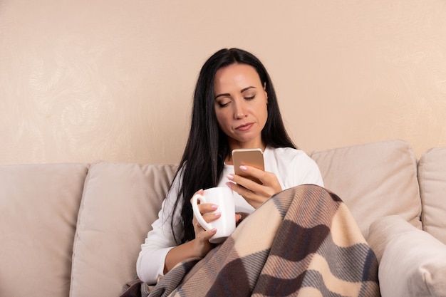 Junge Frau, die eine Tasse Tee auf dem Sofa trinkt