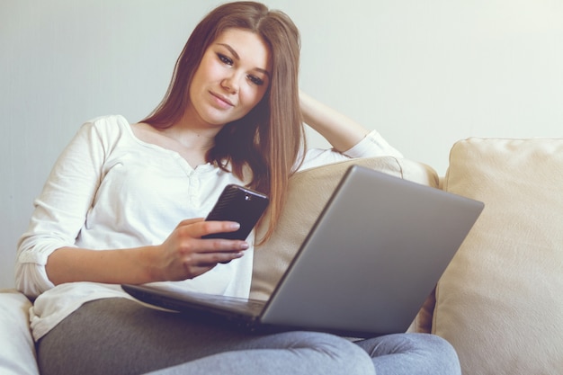 Junge Frau, die einen Laptop auf einem Sofa benutzt