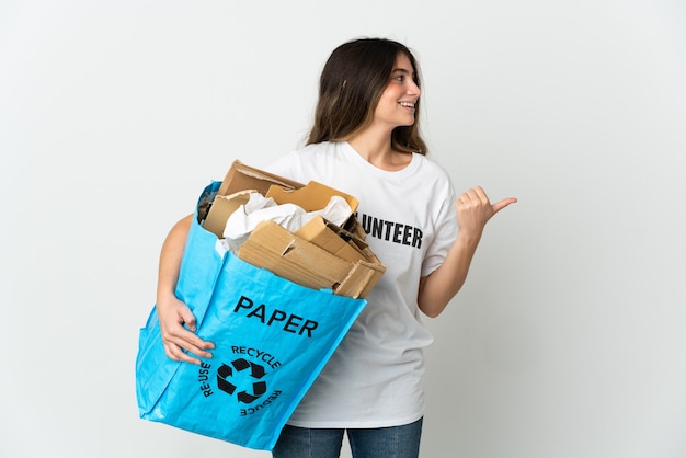 Junge Frau, die einen Recyclingbeutel voll Papier hält, um isoliert auf Weiß zu recyceln, das zur Seite zeigt, um ein Produkt zu präsentieren