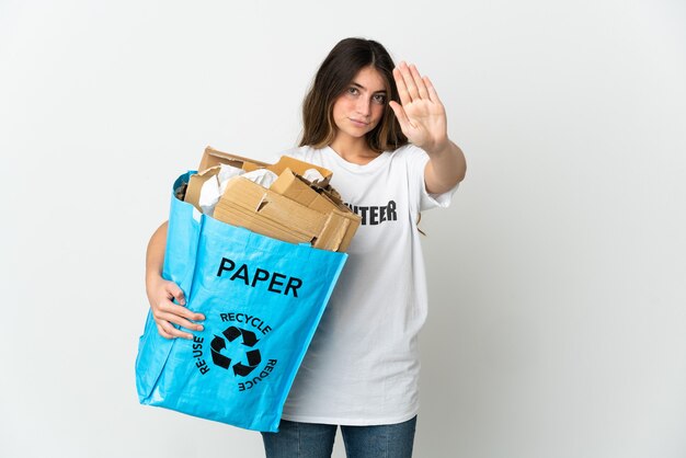 Junge Frau, die einen Recyclingbeutel voll Papier hält, um lokalisiert auf weißer Wand zu recyceln, die Stoppgeste macht