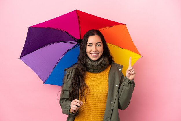 Junge Frau, die einen Regenschirm lokalisiert auf rosa Hintergrund hält, der eine große Idee aufzeigt