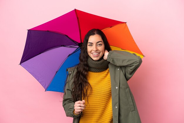 Junge Frau, die einen Regenschirm lokalisiert auf rosa Hintergrund lachend hält