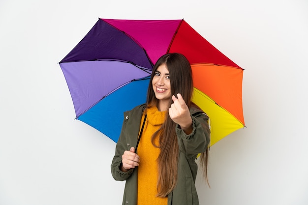 Junge Frau, die einen Regenschirm lokalisiert auf weißer Wand hält, die kommende Geste tut