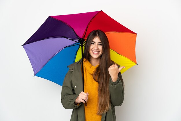 Junge Frau, die einen Regenschirm lokalisiert auf weißer Wand hält, die zur Seite zeigt, um ein Produkt zu präsentieren