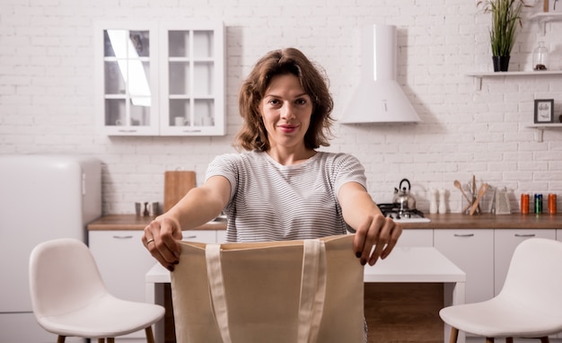 Foto junge frau, die einen stoffbeutel hält. in der küche. ich bin kein plastik. kampagne zur reduzierung des einsatzes von plastiktüten. kein verlust