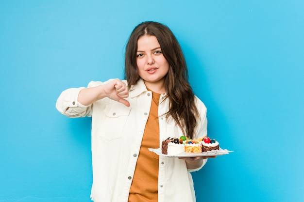 Foto junge frau, die einen süßen kuchen hält, der eine abneigungsgeste zeigt, daumen nach unten