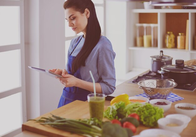 Junge Frau, die einen Tablet-Computer verwendet, um in ihrer Küche zu kochen