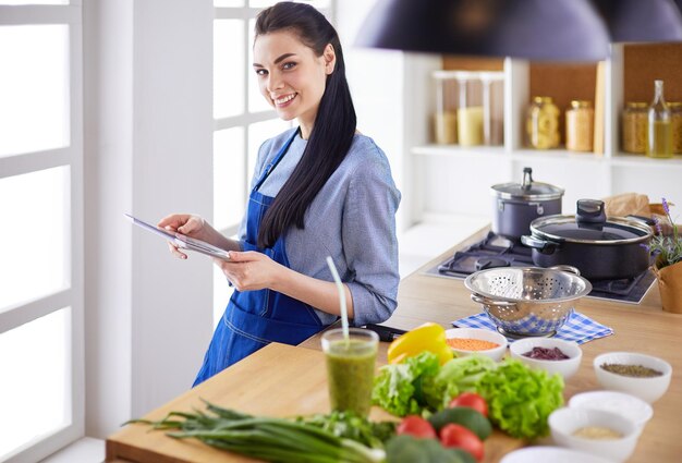 Junge Frau, die einen Tablet-Computer verwendet, um in ihrer Küche zu kochen