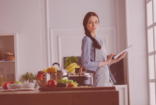 Junge Frau, die einen Tablet-Computer verwendet, um in ihrer Küche zu kochen