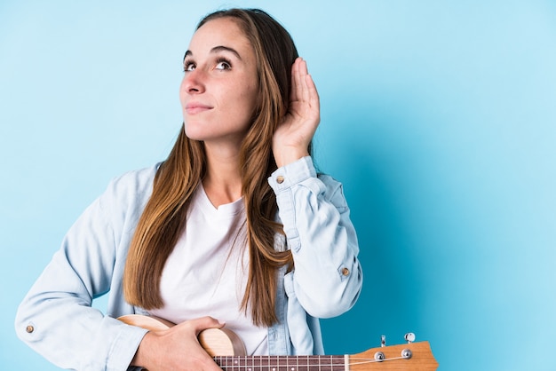 Junge Frau, die einen Ukelele versucht, einen Klatsch zu hören hält