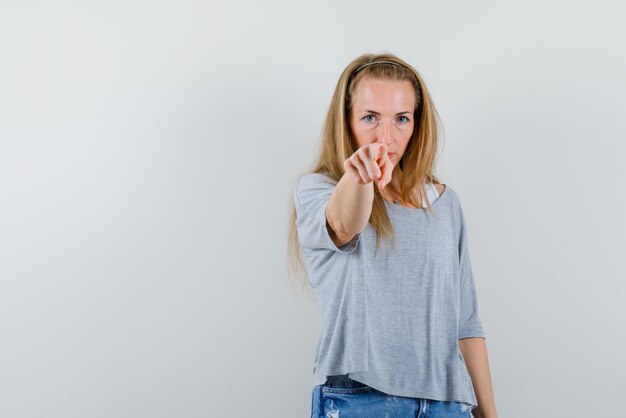 Junge Frau, die etwas mit ihrem Finger auf weißem Hintergrund zeigt