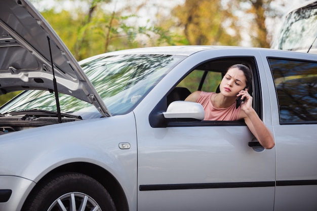 Junge Frau, die Evakuierungsdienst anruft. Ihr Auto hatte auf der Straße eine Panne.