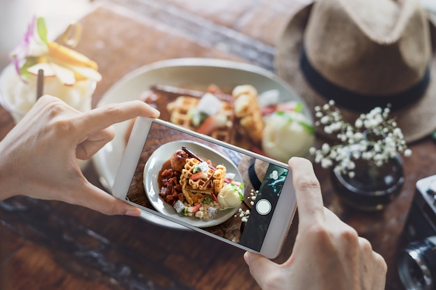 Junge Frau, die Foto des Lebensmittels mit intelligentem Telefon im Restaurant macht