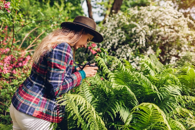 Junge Frau, die Fotografien auf Kompaktkamera im Sommergarten nimmt. Glückliches Mädchen, das Bilder des Farns im Park macht, der Natur genießt