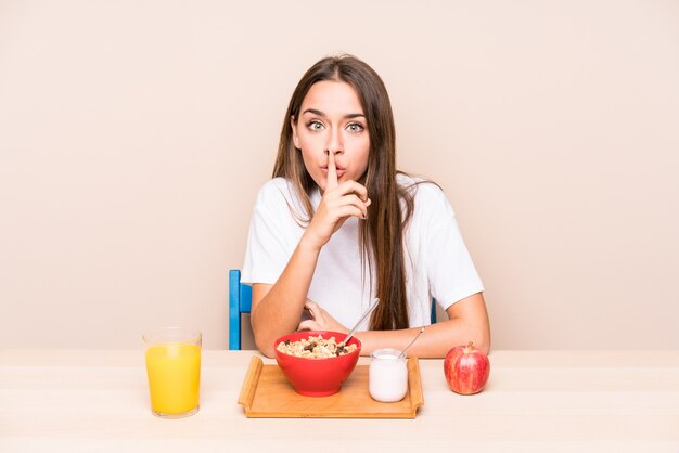 Junge Frau, die frühstückt, ein Geheimnis halten oder um Ruhe bittet