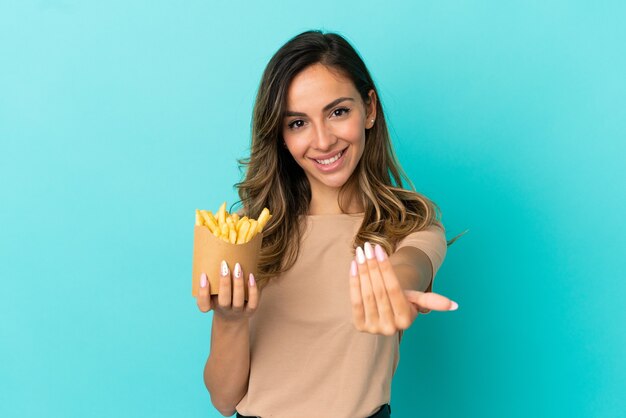 Junge Frau, die gebratene Chips über isoliertem Hintergrund hält und einlädt, mit der Hand zu kommen. Schön, dass du gekommen bist
