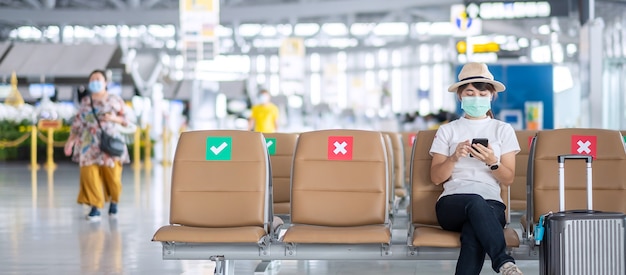 Junge Frau, die Gesichtsmaske trägt und mobiles Smartphone im Flughafen verwendet