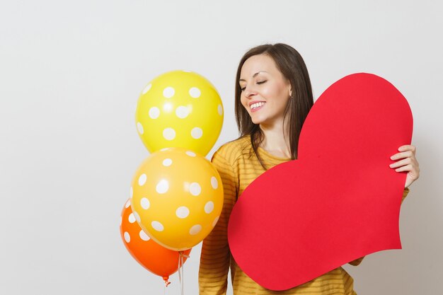 Junge Frau, die großes rotes Herz, gelb-orange Ballons lokalisiert auf weißem Hintergrund hält. Kopieren Sie Platz für Werbung. Mit Platz für Text. Valentinstag- oder Internationaler Frauentag-Konzept.