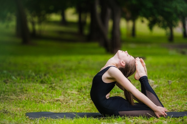 Junge Frau, die Gymnastikyoga tut und im Stadtpark auf Sonnenuntergang streckt