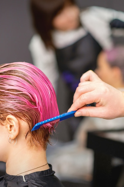 Junge Frau, die Haarbehandlung nach rosa Färbung durch Hand des männlichen Friseurs im Friseursalon erhält