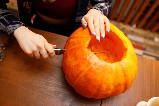 Junge Frau, die Halloween-Kürbis Jack-o-Laterne macht. Weibliche Hände, die Kürbisse mit Messer schneiden.