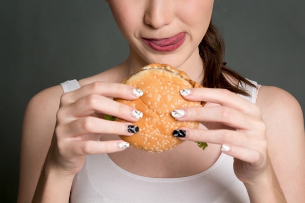 Junge Frau, die Hamburger auf grauem Hintergrund isst