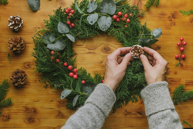 Junge Frau, die handgemachten Weihnachtskranz mit Kiefernkegel verziert Draufsicht