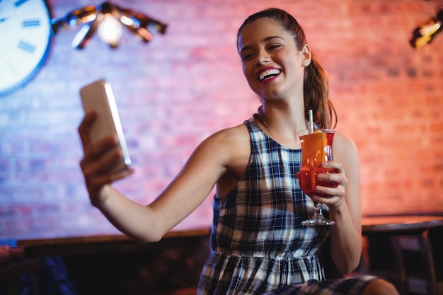 Junge Frau, die Handy beim Cocktailtrinken verwendet