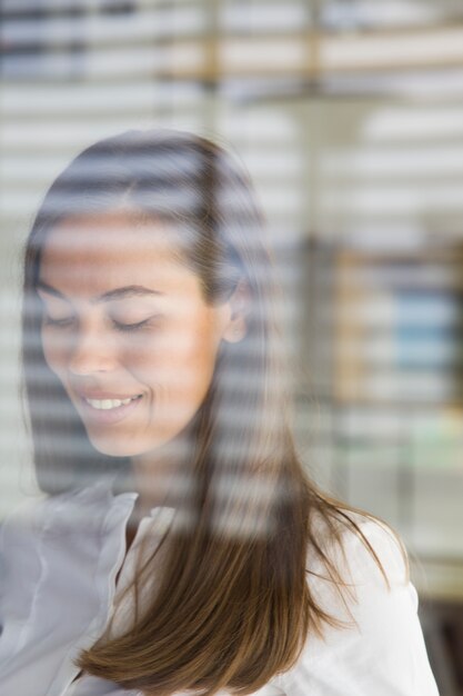 Junge Frau, die Handy hinter dem Glas im Büro verwendet