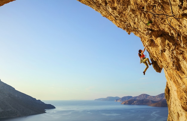 Junge Frau, die herausfordernde Route in Höhle bei Sonnenuntergang, Kalymnos-Insel, Griechenland klettert