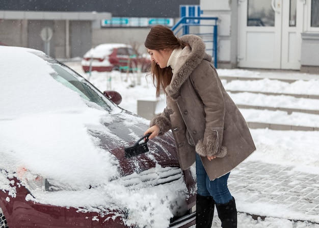 Junge Frau, die ihr Auto nach Schneesturm säubert